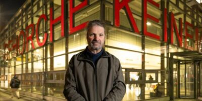 Andreas Kemper steht vor einem verglasten Gebäude und blickt in die Kamera. Auf dem Gebäude sind rote Buchstaben angebracht auf denen steht: Gehorche Keinem. Foto: Rolf Nobel.