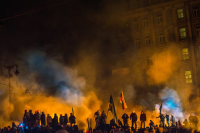 A flag and people in front of smoke and buildings during the Euromaidan protests in Kiev 2014